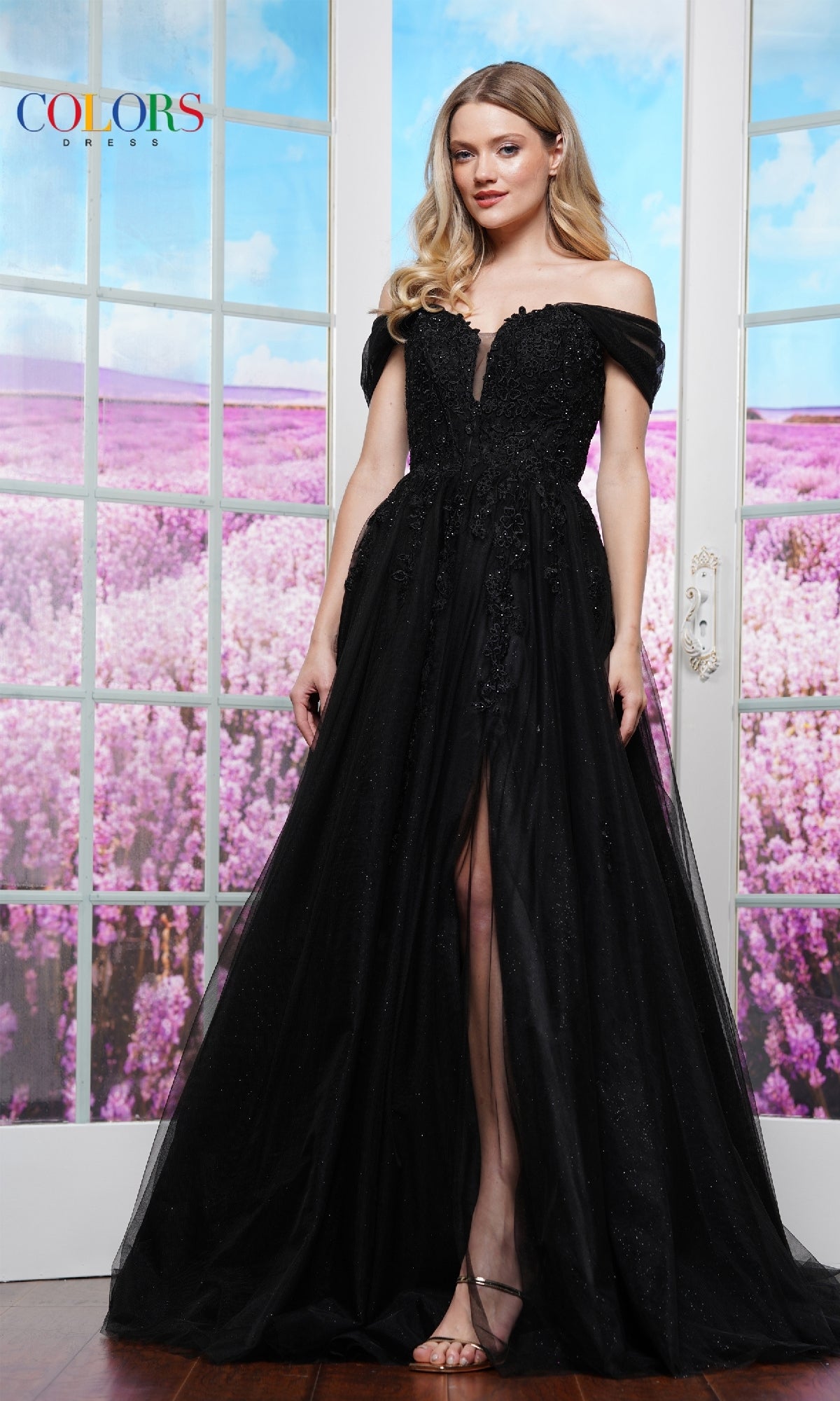 A woman stands before glass doors, wearing the Long Glitter Prom Ball Gown: Colors Dress 3474, as a beautiful lavender field stretches behind her.
